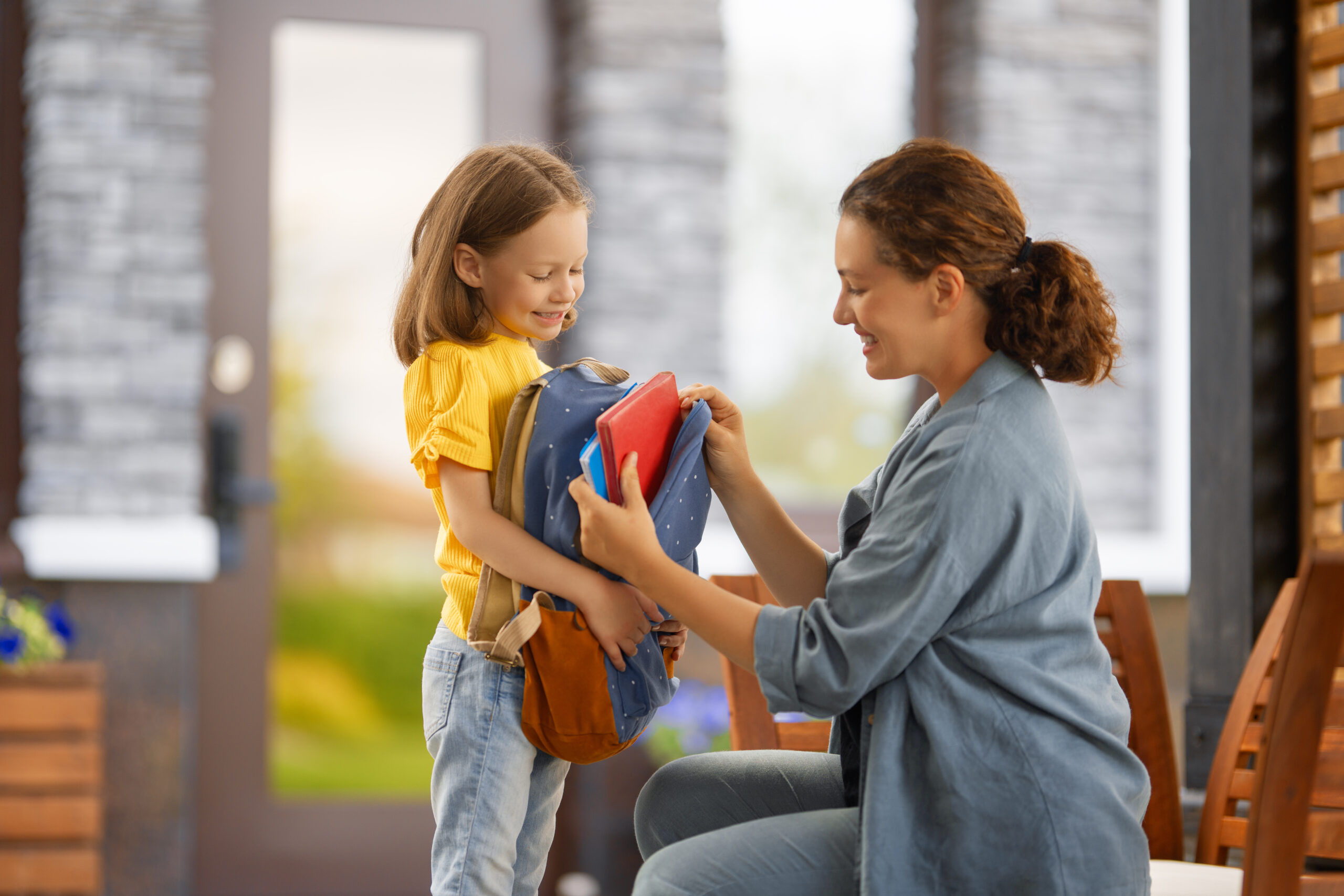 Parent and pupil of primary school going hand in hand. Woman and girl with backpack behind the back. Beginning of lessons.